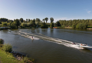 Sciatore d'acqua trainato da motoscafo su lago tranquillo al Vakantiepark Klein Strand, Fiandre Occidentali, Belgio.