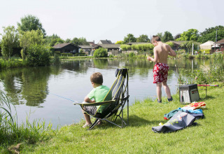 Twee jongens vissen aan het meer bij Vakantiepark Klein Strand, omgeven door groen en vakantiewoningen.