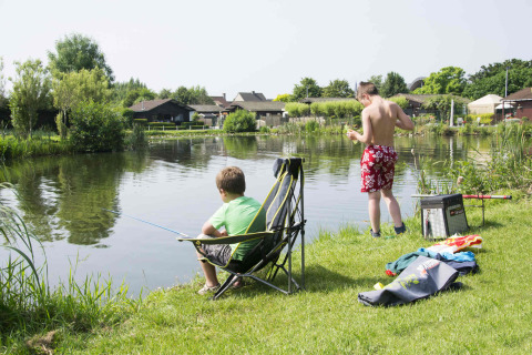 Twee jongens vissen aan het meer bij Vakantiepark Klein Strand, omringd door natuur en vakantiehuisjes.