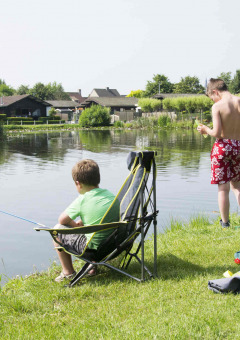 Dos niños pescan junto al lago en Vakantiepark Klein Strand, rodeados de naturaleza y casas de vacaciones.