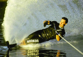 Persoon waterskiet op een meer, grote waterspray bij Vakantiepark Klein Strand in België.