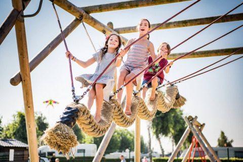 Children playing happily on a large rope climbing structure at Vakantiepark Klein Strand in West Flanders, Belgium.