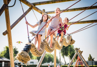 Kinder spielen lachend auf einem großen Seilkletterspielplatz im Vakantiepark Klein Strand, Westflandern.