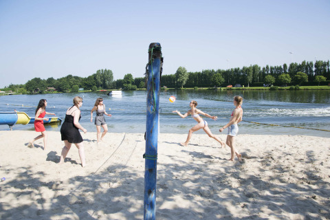 People play beach volleyball on a sandy lakeshore at Vakantiepark Klein Strand, West Flanders, Belgium.