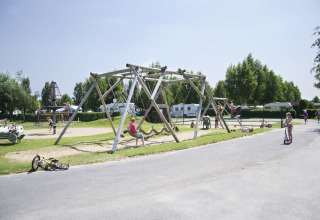 Kinder spielen auf einem Spielplatz mit Schaukeln und Klettergerüsten in einem Ferienpark mit Wohnwagen.