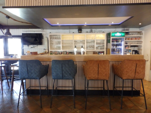 Bar moderne avec quatre chaises rembourrées au Camping Um Bierg, Diekirch, Luxembourg, verres et boissons derrière.