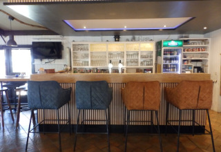 Bar moderne avec quatre chaises rembourrées au Camping Um Bierg, Diekirch, Luxembourg, verres et boissons derrière.