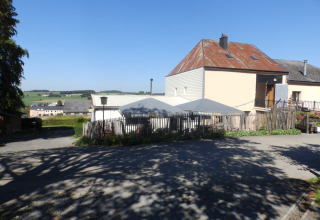Foto van Camping Um Bierg in Diekirch, Luxemburg met gebouwen, parasols en groene landelijke omgeving.