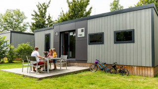 Familia disfruta de una comida al aire libre en Taos XL Delux Mobile Home, Baalse Hei, Bélgica, con bicicletas.