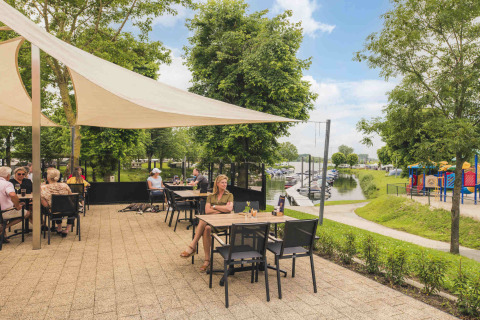 Outdoor terrace dining at MarinaPark Bad Nederrijn, Gelderland, overlooking a marina and colorful playground area.