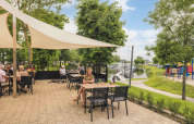 Udendørs terrasse med gæster på MarinaPark Bad Nederrijn, med udsigt til legeplads og bådebro i Gelderland.
