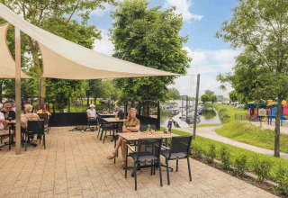 Udendørs terrasse med gæster på MarinaPark Bad Nederrijn, med udsigt til legeplads og bådebro i Gelderland.