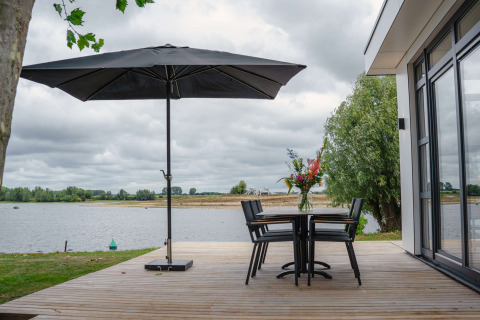Outdoor patio at MarinaPark Bad Nederrijn in Gelderland, Netherlands with lake view, table, chairs, and umbrella.