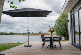 Terrasse extérieure au MarinaPark Bad Nederrijn, en Gelderland, Pays-Bas, avec parasol, table, chaises et vue sur le lac.