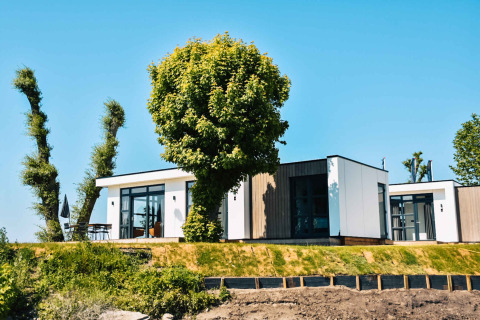 Modernes Ferienhaus im MarinaPark Bad Nederrijn, Gelderland, Niederlande, mit Bäumen und blauem Himmel.