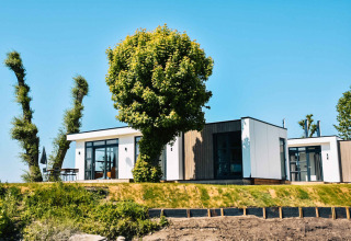 Casa de vacaciones moderna en MarinaPark Bad Nederrijn, Gelderland, Países Bajos, rodeada de árboles y cielo azul.