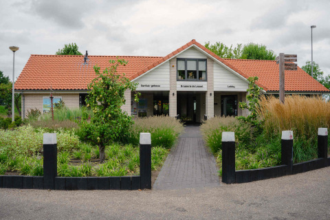 Toegang tot een vakantieparkgebouw met rood dak en tuin bij MarinaPark Bad Nederrijn in Gelderland, Nederland.