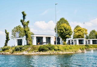 Modern waterfront holiday cottages at MarinaPark Bad Nederrijn, surrounded by greenery and blue water in Gelderland.