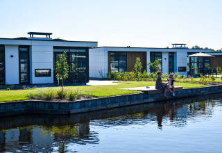Deux personnes sont assises près de l’eau devant des résidences modernes à MarinaPark Residentie Nieuw Loosdrecht.