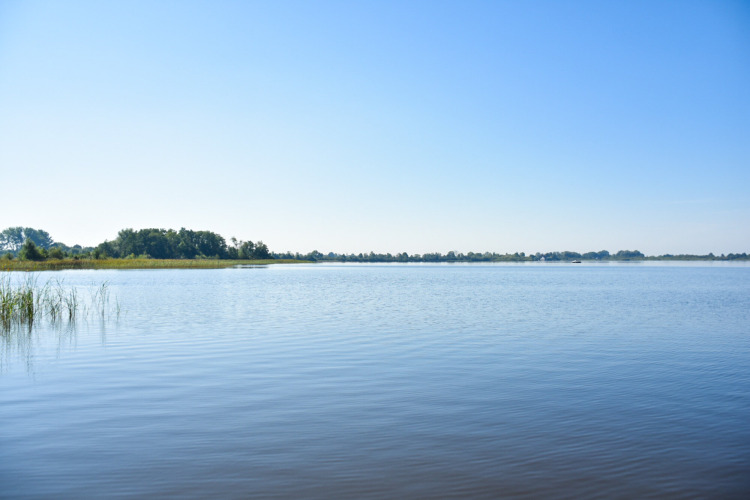 Blick auf einen ruhigen See im MarinaPark Residentie Nieuw Loosdrecht, Nordholland, unter blauem Himmel.