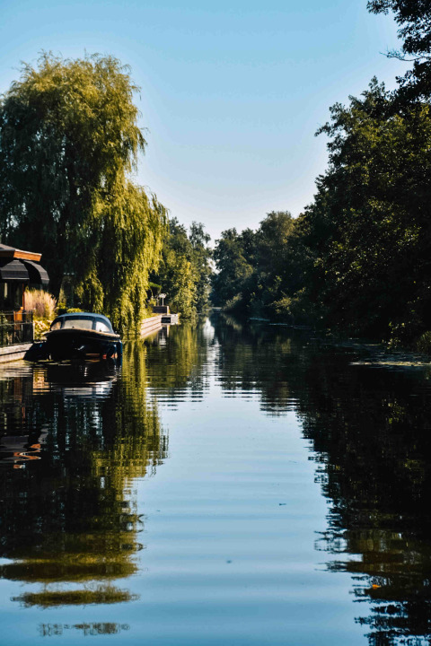 Idyllischer Kanalblick mit Boot, Bäumen und Häusern bei MarinaPark Residentie Nieuw Loosdrecht, Holland.