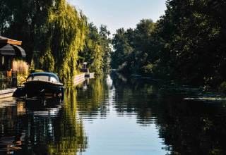 Idyllischer Kanalblick mit Boot, Bäumen und Häusern bei MarinaPark Residentie Nieuw Loosdrecht, Holland.
