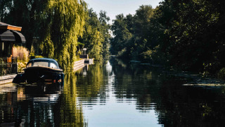 Vista idílica de canal con barco, árboles y casas en MarinaPark Residentie Nieuw Loosdrecht, Países Bajos.