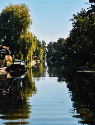 Vista idílica de canal con barco, árboles y casas en MarinaPark Residentie Nieuw Loosdrecht, Países Bajos.