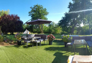 Hyggelig terrasse med havemøbler og parasol i grønne omgivelser på Camping d'Artagnan, Occitanie, Frankrig.