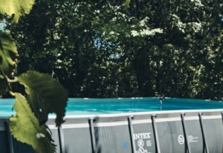 An above-ground swimming pool with wooden steps surrounded by trees at Camping d'Artagnan, Occitanie, France.
