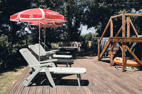 Sdraio e ombrelloni rossi su terrazza di legno al Camping d'Artagnan in Occitania, Francia, tra gli alberi.
