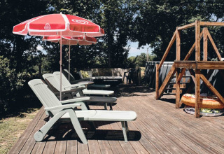 Sdraio e ombrelloni rossi su terrazza di legno al Camping d'Artagnan in Occitania, Francia, tra gli alberi.