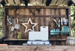Cucina esterna con fornello a gas, parete in legno, utensili e piatti blu al Camping d'Artagnan in Occitania.