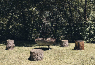 Udendørs bålplads omgivet af træstubbe som siddepladser i grønt område ved Camping d'Artagnan, Occitanie.