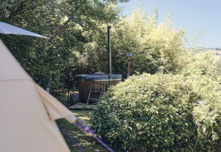 Vasca idromassaggio all'aperto e tenda immersi nel verde al Camping d'Artagnan, Occitania, Francia.