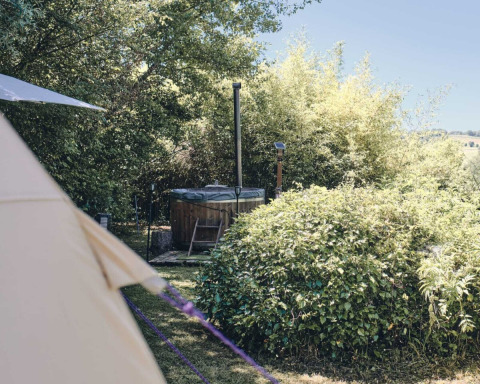 Foto eines holzverkleideten Whirlpools und Zeltes inmitten von Bäumen im Camping d'Artagnan, Occitanie, Frankreich.