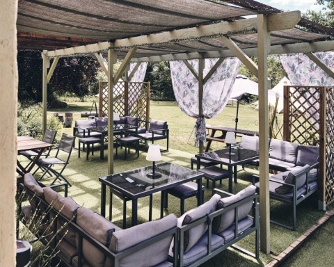 Area lounge all'aperto al Camping d'Artagnan, Occitania, Francia, con divani, tavoli e tende ombreggianti.