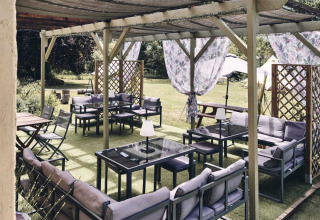 Buitenzitruimte bij Camping d'Artagnan, Occitanië, Frankrijk met banken, tafels en schaduwdoeken.