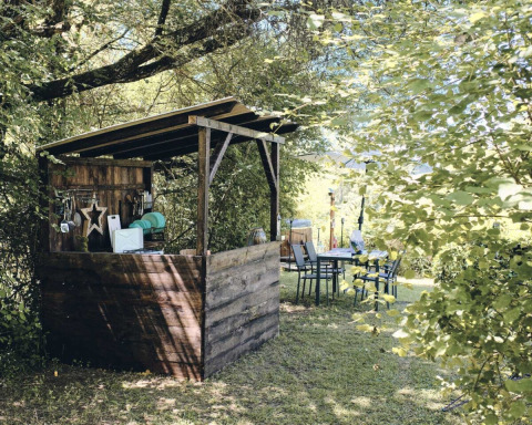 Refugio de madera y mesa exterior rodeados de naturaleza en Camping d'Artagnan, Occitania, Francia.