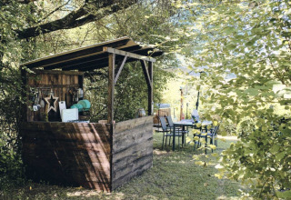 Udendørs træskur og spiseplads i grønne omgivelser, Camping d'Artagnan, feriepark i Occitanie, Frankrig.