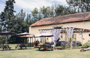 Udendørs siddeområde med parasoller og træborde foran en rustik bygning ved Camping d'Artagnan, Occitanie.