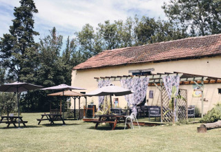 Area all'aperto con tavoli da picnic, ombrelloni ed edificio rustico al Camping d'Artagnan in Occitanie.
