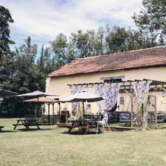 Espace extérieur avec tables, parasols et bâtiment rustique au Camping d'Artagnan, Occitanie, France.