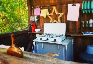 Cucina all'aperto con fornello, piatti e macchina da caffè al Camping d'Artagnan, Occitania, Francia.