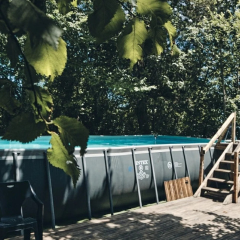 Piscina esterna fuori terra e terrazza in legno circondate da alberi al Camping d'Artagnan in Occitania.
