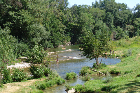 Des personnes profitent de la rivière bordée d’arbres au Slow Village Provence Occitane, en Occitanie.