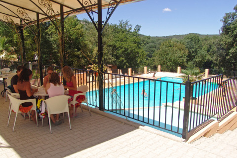 Personas sentadas bajo una terraza sombreada junto a una piscina vallada en Slow Village Provence Occitane, Francia.
