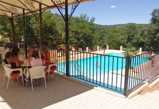 Persone sedute sotto una terrazza ombreggiata accanto alla piscina recintata di Slow Village Provence Occitane, Francia.