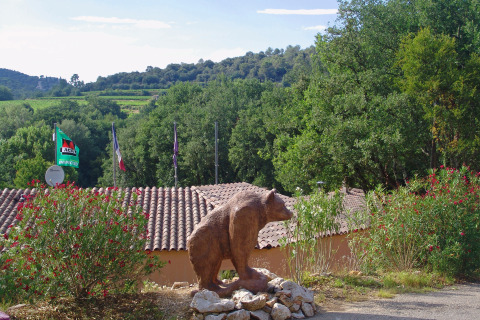 Vista del parque vacacional Slow Village Provence Occitane en Occitania, Francia, con escultura de oso y vegetación.