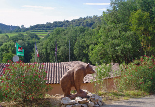 View of Slow Village Provence Occitane holiday park in Occitanie, France, with bear sculpture and greenery.